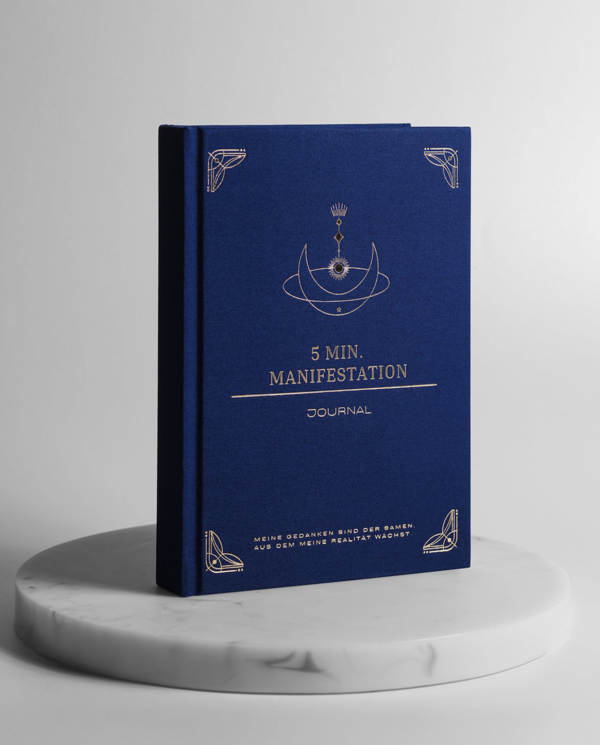 Blaues 5 Minuten Manifestation Journal mit goldener Prägung auf einem runden Marmorsockel, hochwertiges Hardcover Tagebuch für Journaling, Achtsamkeit und bewusste Manifestation.