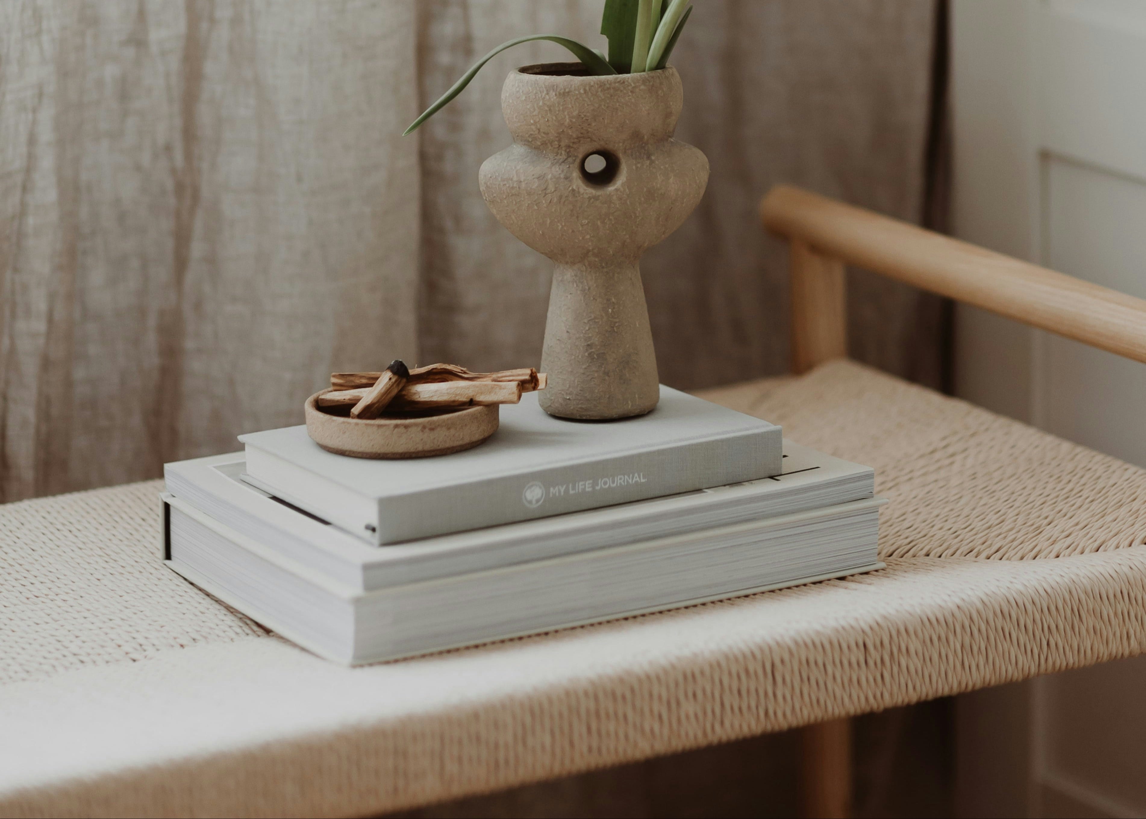 Palo Santo Räucherholz in einer Schale auf Journals mit Pflanze in ruhiger Umgebung.