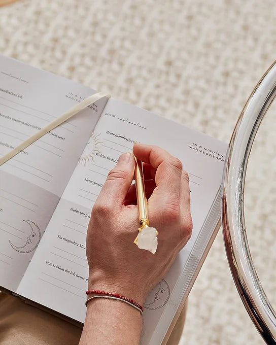 person schreibt mit goldenem kristall stift und bergkristall in manifestation journal ästhetisches journaling ritual warme sonnenstrahlen minimalistisches selfcare setup spirituelles schreiben luxuriöse stationery myspiritclub