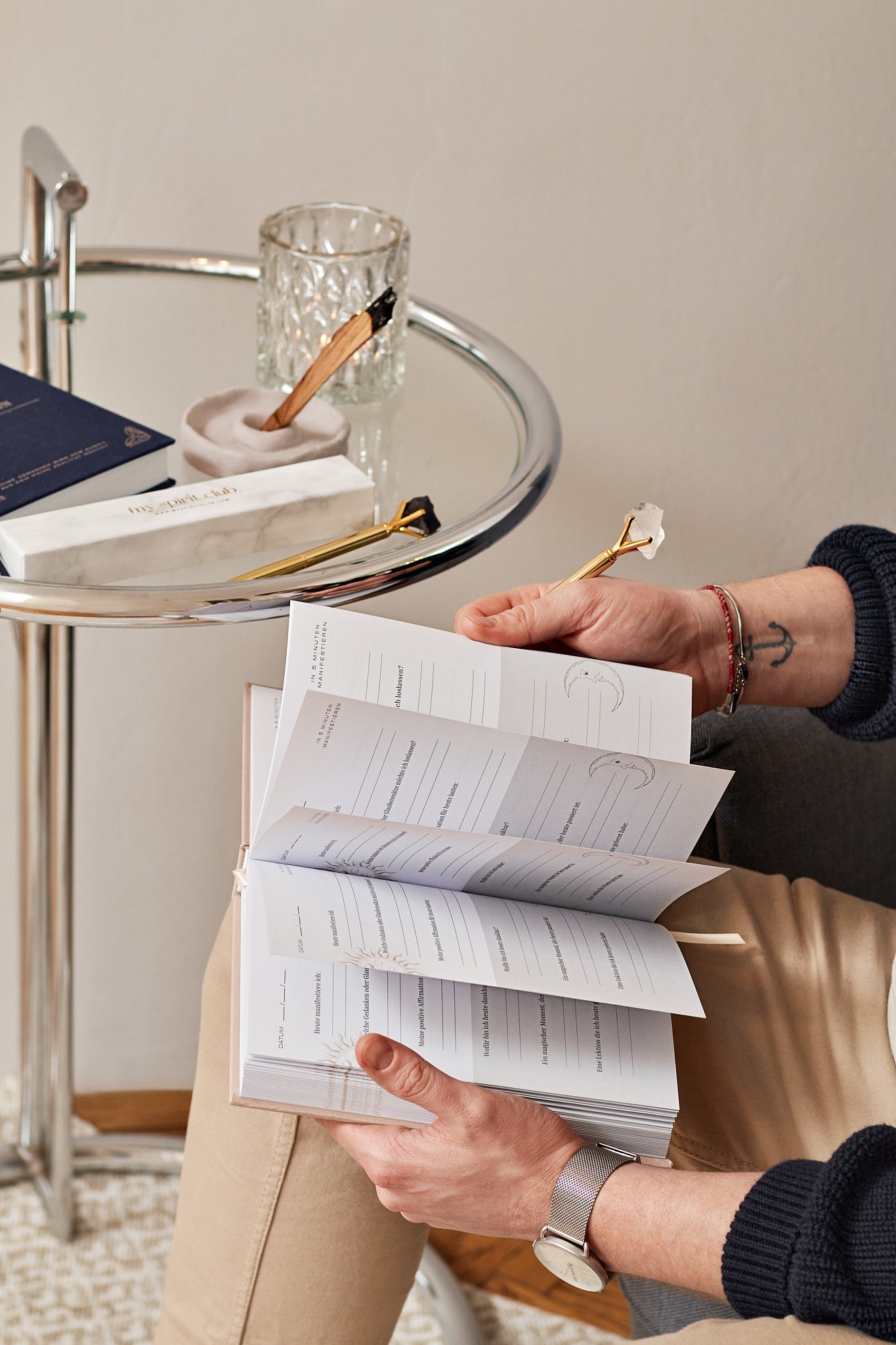 Hand schreibt in einem hellen Raum an einem schönen Beistelltisch in sein 5 Minuten Manifestation Journal und blättert sich durch das Journal.