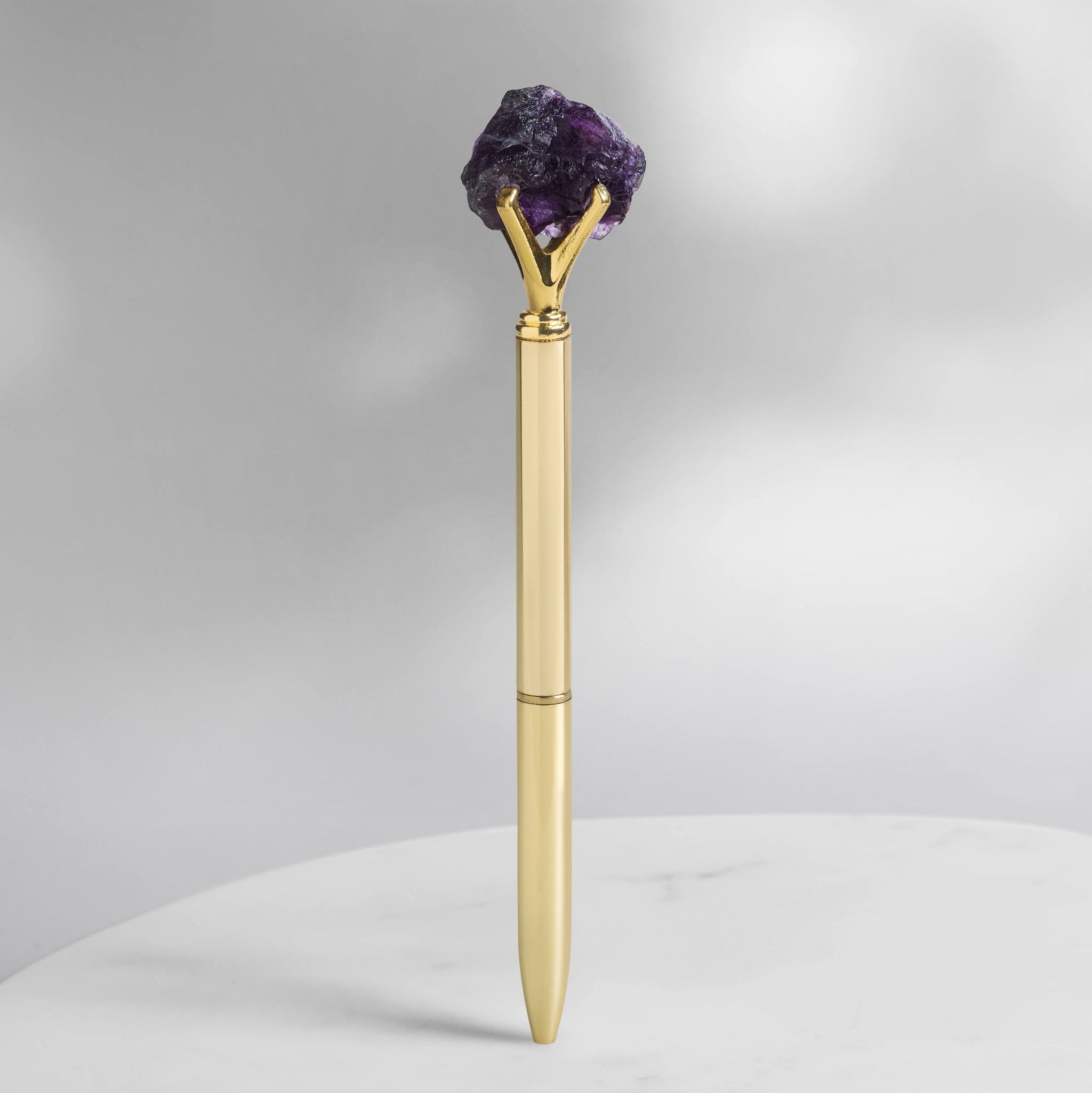 Fluorit Kristallstift in Goldoptik mit rohem violettem Fluorit, Schutz- und Fokus-Kristall für Journaling, Manifestation und tägliche Rituale auf hellem Hintergrund.
