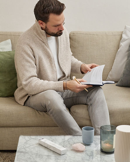 Mann schreibt im 5 Minuten Manifestation Journal mit Kristallstift auf dem Sofa
