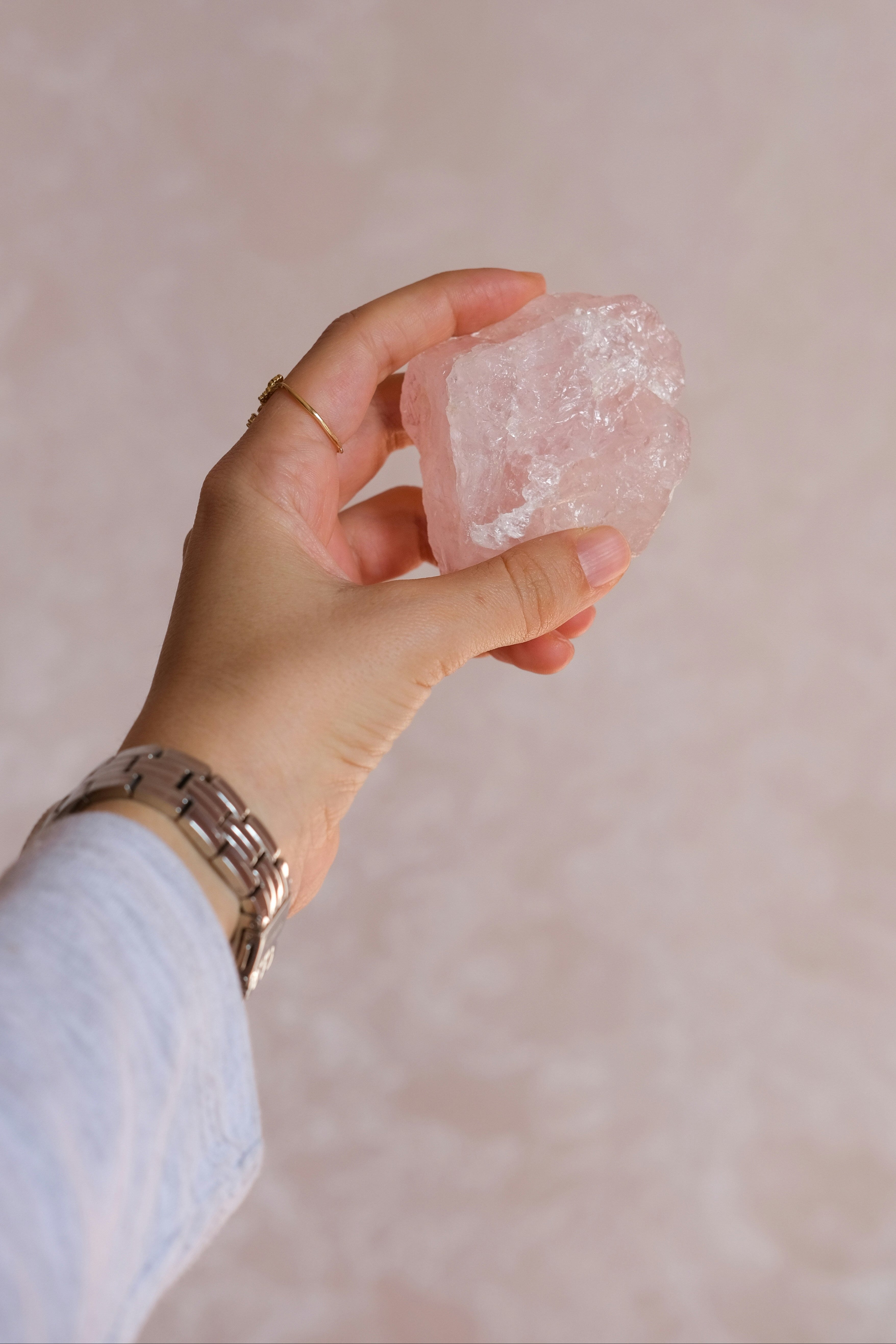 Hand hält einen rohen Rosenquarz-Kristall in zartem Rosa: Symbol für Selbstliebe, Harmonie und liebevolle Energie.